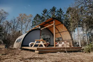 Arcade: curved-roof glamping tent with a deck and a picnic table, in the forest